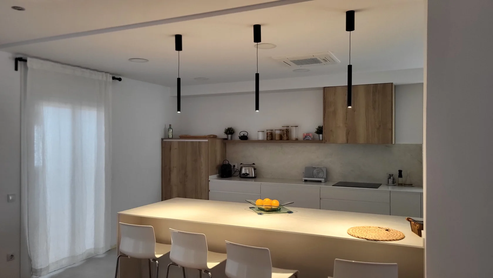 Cocina con isla, lámparas colgantes y climatización de cassette integrada en el techo, un trabajo de Garrido Serveis