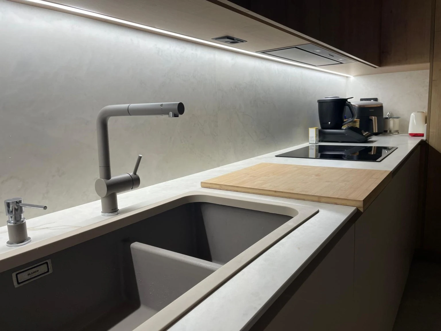 Cocina con tira LED bajo los armarios, encimera clara y grifo gris