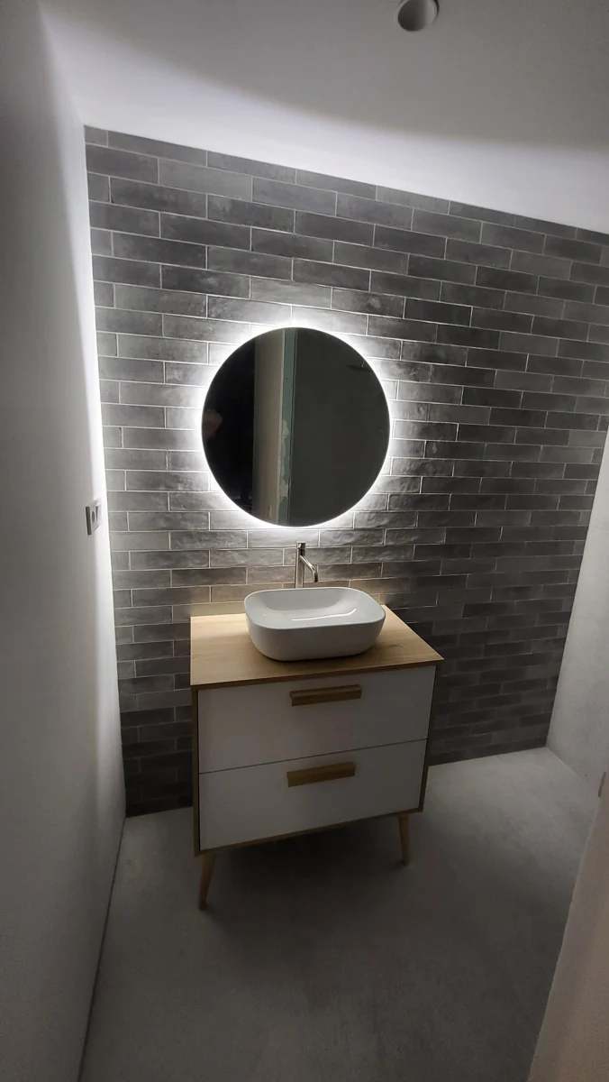 Lavabo sobre mueble de madera y espejo redondo retroiluminado